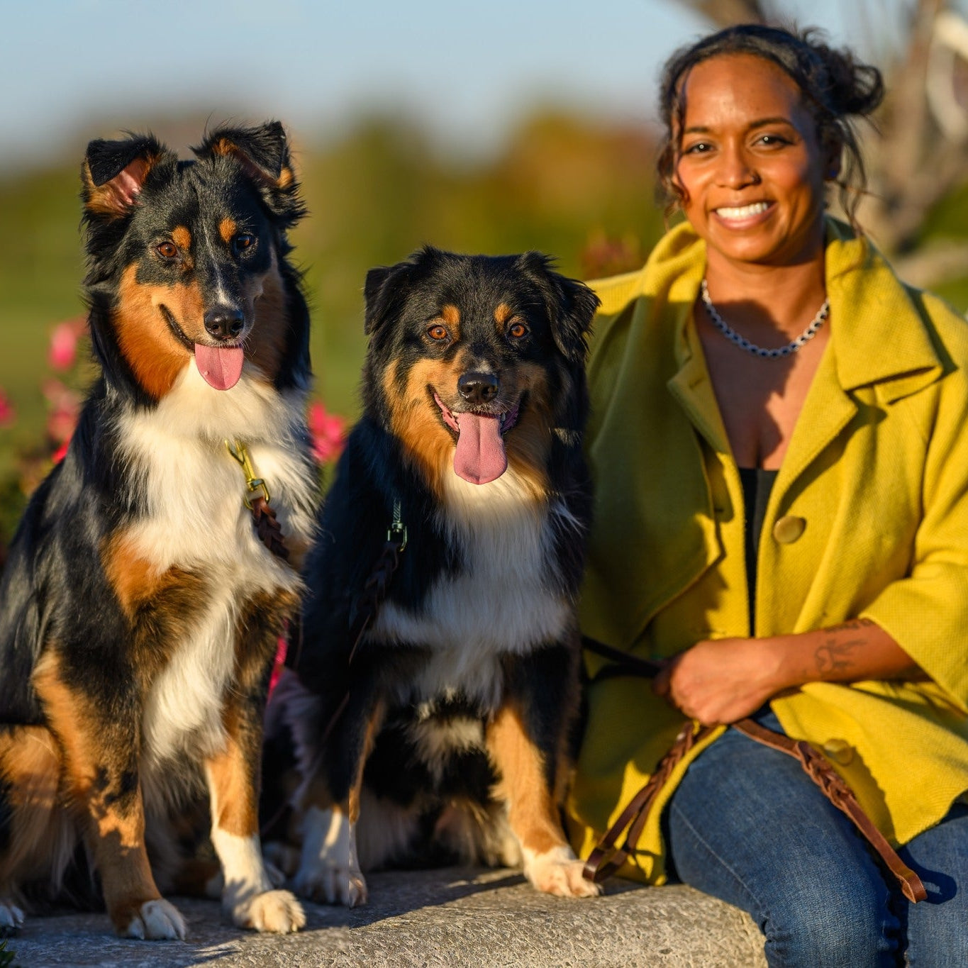 Woman in a yellow coat sitting with two dogs in a garden setting