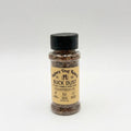 A bottle of Buck Dust dog topper by Rainey Dog Ranch, featuring a tan label and a black cap, set against a plain light gray background.